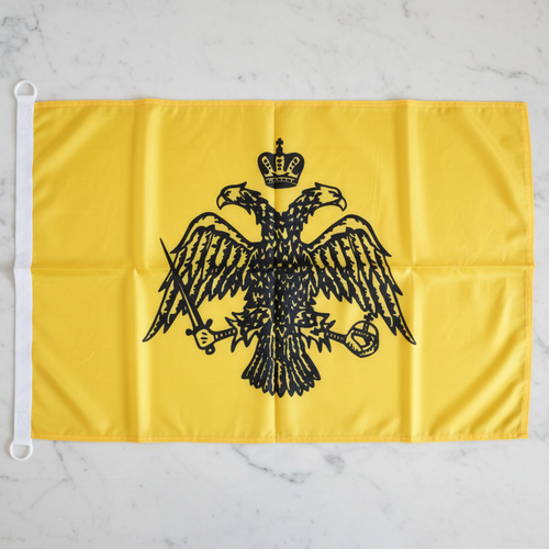 Byzantinische Flagge mit Doppeladler – goldgelber Fahnenstoff mit schwarzem Doppeladler und Krone, auf Marmor liegend, Ösen sichtbar