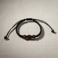 Makramee-Armband im Komboskini-Stil – schwarz mit Holzkreuz IC XC NIKA und Holzperlen, Flat Lay auf Leinenstoff